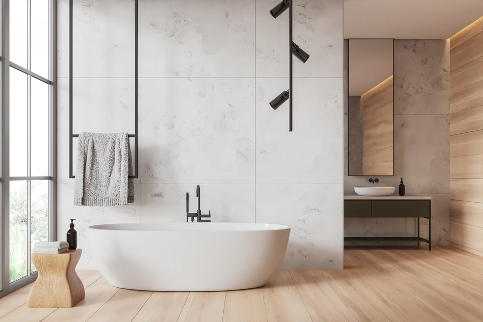 Salle de bain moderne avec baignoire îlot blanche, carrelage beige grand format au sol et mur, plafond béton brut